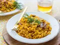 Delicioso arroz con setas y carne, servido en plato blanco con tenedor dorado y ramita de romero.