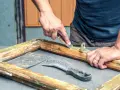 Uomo usa raschietto per rimuovere vecchia vernice da telaio in legno, mostrando come sverniciare il legno con attrezzi.
