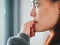 Une jeune femme se ronge les ongles, un signe de stress ou d'anxiété. La signification psychologique de se ronger les ongles est souvent liée à une recherche de réconfort.