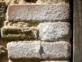 Mur en briques anciennes couvert de salpêtre, la pierre et le bois se côtoient.