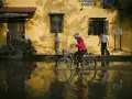 Une femme à vélo traverse une rue inondée, reflétant la vie quotidienne. Quel objectif pour photo de rue capture cette scène ?