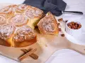 Ein köstliches Zimtschnecken Rezept: goldbraune, mit Nüssen und Puderzucker bestreute Schnecken auf einem Holzbrett, daneben Zimtstangen und Haselnüsse.