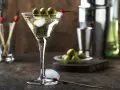Elegancki martini z oliwką, gotowy do degustacji. Obok kostki lodu i talerzyk z oliwkami.