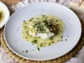 Un delicioso bacalao en salsa verde, con perejil fresco picado y trozos de pan al lado.