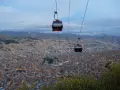 Red la paz gondola cabins glide over a sprawling city at dusk, with lights twinkling below and mountains in the distance.