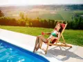 Donna rilassata su una sdraio, con drink, vicino a una piscina. Il sole splende, ideale per chi vuole sapere come abbronzarsi velocemente.