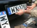 Montaż nowych tablic rejestracyjnych. Jedna z nich, z numerem WX 37808, jest właśnie wkładana. Obok leży kolejna, jeszcze w folii.