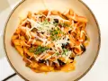 Penne z bogatym sosem anchois, czarnymi oliwkami i parmezanem, udekorowane świeżym tymiankiem.