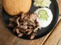 Ein Teller mit gegrilltem Fleisch, einem Brötchen, Tzatziki und Krautsalat. Perfekt für ein leckeres Gyros Rezept.