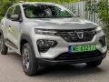 Srebrna Dacia Spring z zieloną tablicą rejestracyjną WE 632YJ, przód samochodu.
