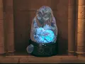 Figura de hielo con energía azul brillante, como el hombre de las lunas en Hogwarts Legacy, sobre un pedestal decorado.
