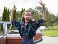 Millie Bobby Brown w kolorowej koszuli i szelkach, radośnie pozuje przy samochodzie. Jej filmy, seriale i programy to gwarancja emocji!