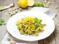 Makaron orecchiette z zielonym pesto, pistacjami i skórką cytrynową na białym talerzu.