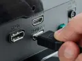 Hand steckt HDMI-Kabel ein, um den PC mit dem Fernseher zu verbinden. Anschlüsse für DisplayPort und HDMI sind sichtbar.