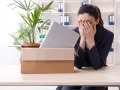 Verzweifelte Frau mit Karton und Laptop im Büro. Sie muss eine innerbetriebliche Versetzung ablehnen und ist sichtlich mitgenommen.
