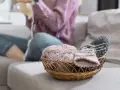Koszyk z włóczką i drutami. Czy farba do tkanin się spiera? Kobieta w swetrze dzierga na drutach.