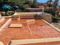 Proceso de impermeabilizar terraza con acabado de tejas rojas. El sol brilla sobre la superficie mojada, lista para proteger la casa.
