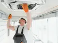 Técnico revisa aire acondicionado en techo, una señal para saber si le falta gas al aire acondicionado es que no enfría.