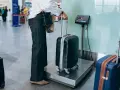Osoba ważąca bagaż rejestrowany na wadze w terminalu lotniczym.