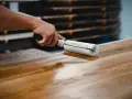 Application d'une finition sur un plateau en bois de manguier, assurant son entretien et sa beauté.
