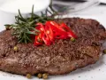 Soczysty stek z airfryer, przyprawiony pieprzem i podany z gałązką rozmarynu, plasterkami chili i zielonym pieprzem.