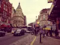 Tętniące życiem ulice Soho w Londynie, z charakterystyczną architekturą, autobusami i ludźmi spacerującymi po chodniku.