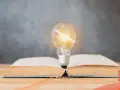 Żarówka nad otwartą książką symbolizuje idealne światło do czytania, które rozjaśnia wiedzę i inspiruje.