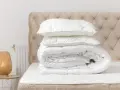 Edredón blanco doblado con almohadas encima, listo para lavar edredón en lavadora. Cabecero acolchado y lámpara de mimbre.