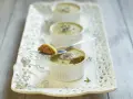 Trois ramequins de foie de volaille, ornés de champignons et de persil, sur un plateau ajouré. Une cuillère présente une bouchée de ce délice.