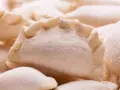 Zbliżenie na grupę surowych, mrożonych pierogów z widocznym, pofałdowanym brzegiem.