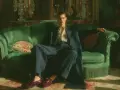 Giovane uomo con abito blu e camicia fantasia, seduto su un divano verde smeraldo, indossa un elegante abito con mocassino bordeaux.