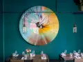 Ein bunter, runder Kunst-Splash ziert die Wand einer stilvollen Werkstatt in Berlin. Tische sind gedeckt, bereit für Gäste.