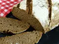 Ein rustikales tschechisches Brot, frisch aufgeschnitten, mit einer kräftigen Kruste und einer saftigen Krume. Daneben liegt eine rot-weiß karierte Serviette.