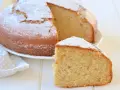 Una fetta di torta di banane sofficissima, cosparsa di zucchero a velo, accanto alla torta intera su un piatto bianco.