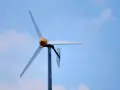 Biała elektrownia wiatrowa z żółtym elementem na środku, na tle błękitnego nieba z chmurami.