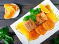 Delicioso salmón a la naranja, servido con rodajas de naranja y hojas de albahaca fresca.