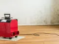 Roter Bautrockner im Einsatz gegen Wasserschaden. Die Wand zeigt deutliche Spuren von Feuchtigkeit und Schimmel.