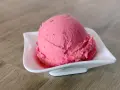 Ein Löffel cremiges Himbeersorbet in einer weißen Schale auf Holzhintergrund.