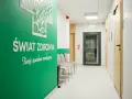 Zielona ściana z napisem "Świat Zdrowia" i logo, korytarz kliniki medycznej z drzwiami i krzesłami.
