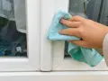 Hand reinigt mit blauem Tuch den weißen Rahmen eines Kunststofffensters.
