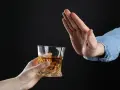 Dłoń odrzuca szklankę z bursztynowym płynem. Pytanie: czy po znieczuleniu u dentysty można pić alkohol?