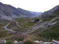 Strada tortuosa che sale verso il colle dei morti, tra montagne verdi e rocciose. Due ciclisti affrontano le curve.