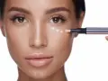 Application de correcteur pour camoufler un cerne bleu. Le pinceau dépose des points de produit sous l'œil.