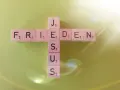 Buchstabensteine bilden ein Kreuz mit den Wörtern "FRIEDEN" und "JESUS". Ein Zitat aus Johannes 14.