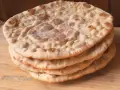 Una pila di pane naan senza lievito, dorato e soffice, su un tagliere di legno.