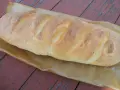 Złocista bułka paryska, świeżo upieczona, leży na papierze do pieczenia na drewnianym stole.