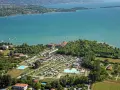 Widok z lotu ptaka na camping Baia Verde nad turkusowym jeziorem, z basenami i licznymi namiotami.