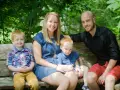 Rodzina na ławce w parku. Dwóch rudowłosych chłopców, mama i tata uśmiechają się. Młodszy syn, jakby w uporczywe naśladowanie innych dzieci, siedzi na kolanach mamy.