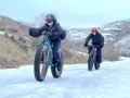 Two people ride fat tire bikes on a snowy path, demonstrating what are fat tire bikes for: tackling challenging winter terrain with their wide tires.