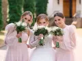Trzy uśmiechnięte kobiety z bukietami kwiatów. Panna młoda w białej sukni i dwie druchny w różowych sukienkach.
